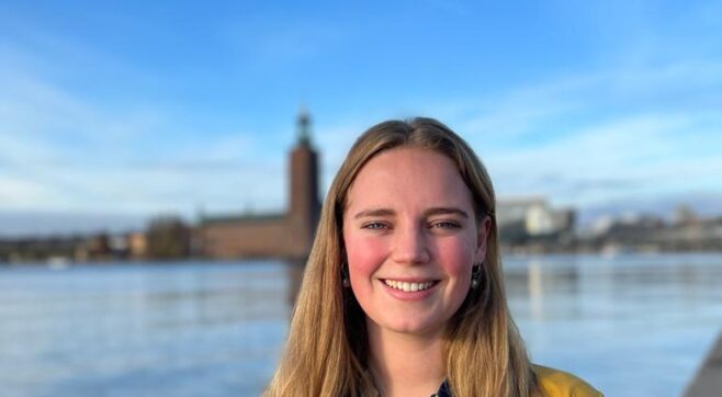 Michelle van Ardenne står framför vattnet med Stockholms stadshus i bakgrunden en solig dag.